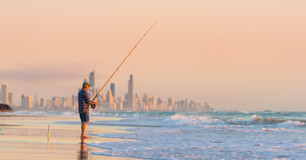Man fishing on gold coast beach with surfers paradise high-rises in the background.  