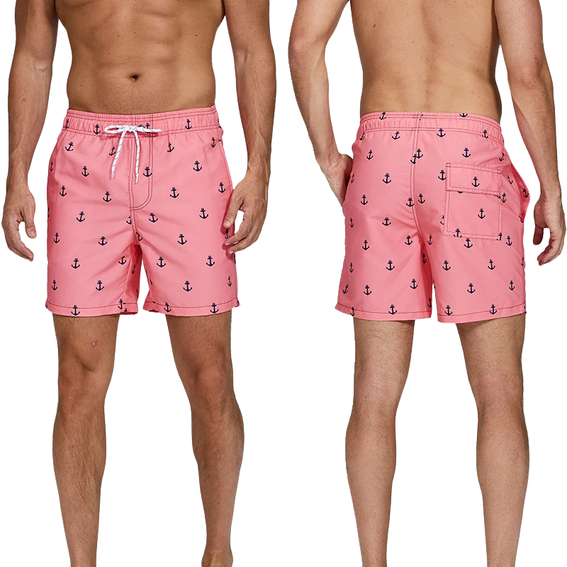 Male model wearing a pair of pink swim shorts with blue boat anchor print on white background. 