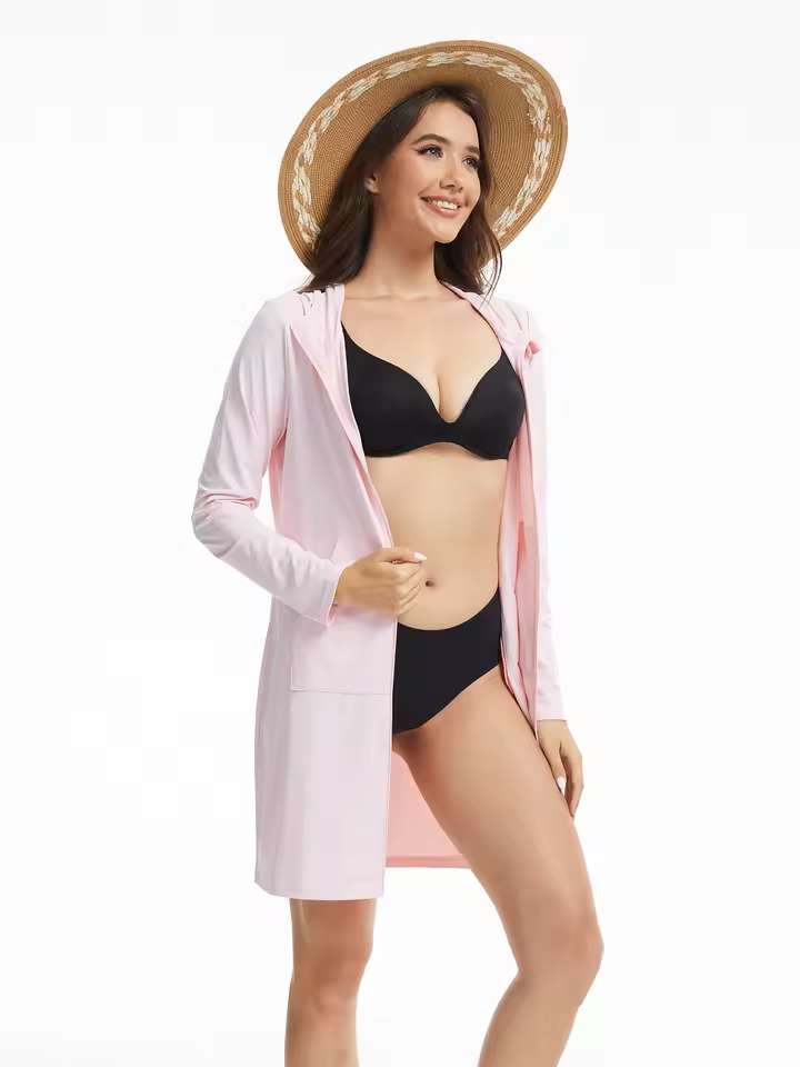Woman wearing a black bikini and pink cover-up with a straw hat on a white background.