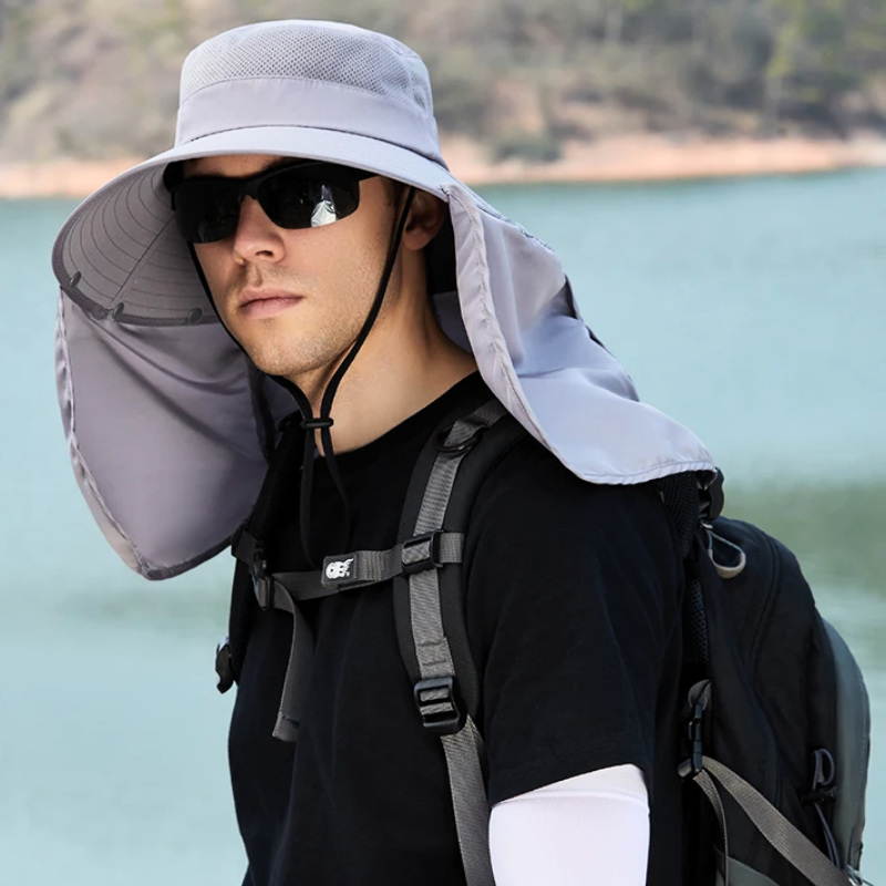 A man hiking by a lake wearing a sun protection fishing hat and black sunglasses. 