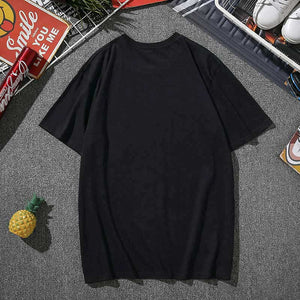 The back of a black cotton t-shirt laying on grey carpet framed around general household items. 