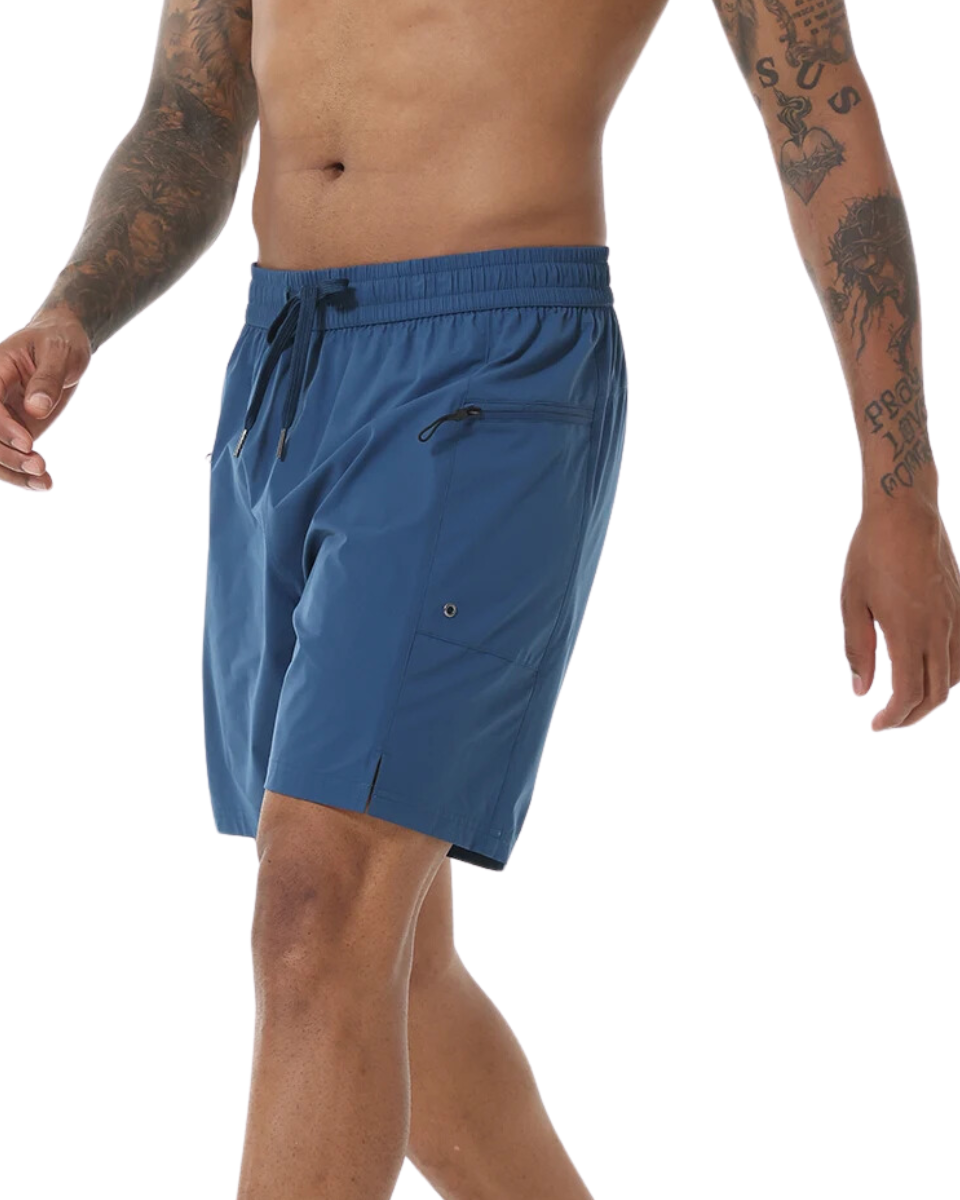 Man wearing blue swim shorts that have zip-up pockets, an elastic waistband and drawstring. The man has several tattoos on his arms. 
