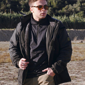Man hiking in the woods wearing a warm black jacket and stylish sunglasses.