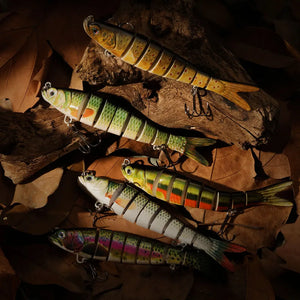 A collection of swimbait lures on brown leaves and logs. 