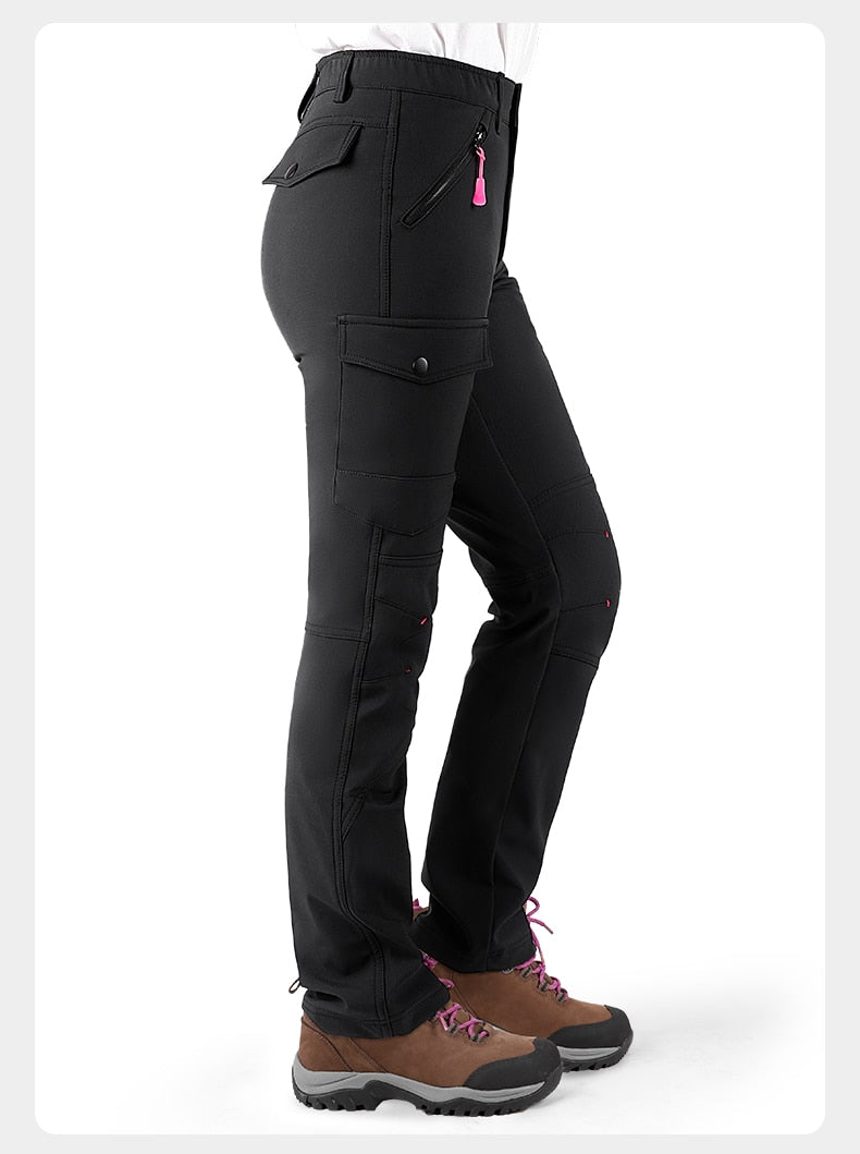 Women's waterproof fleece lined pants for wearing in winter. The female model is standing sideways to show the deep cargo pockets on the side of leg and on the back.