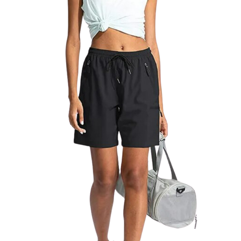 Black zip pocket sports shorts being worn by a female model holding a grey sports bag.