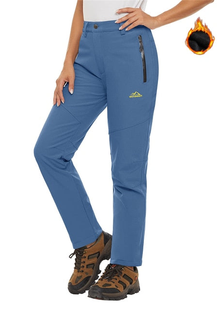 Women wearing light blue waterproof pants, hiking shoes and white shirt. The pants look warm and they have zip pockets.