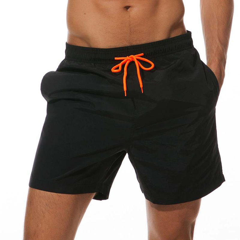 Man wearing a pair of black swimming shorts with orange drawstring.