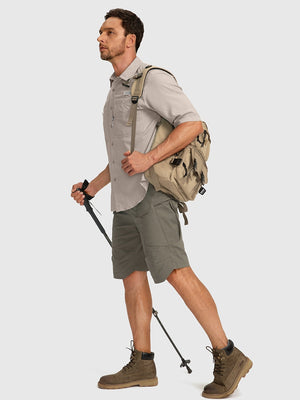 Man wearing a khaki shirt used for hiking and fishing. The shirt has short sleeves. The man is also wearing green hiking shorts and brown hiking shoes while holding a hiking pole.