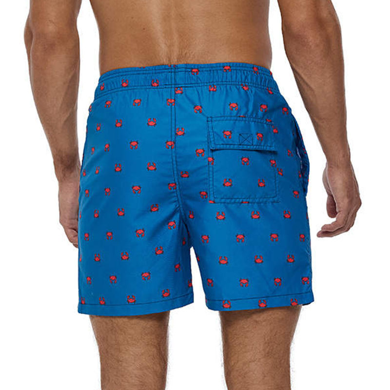 A man wearing a blue pair of shorts  with red crabs. One Velcro pocket on the back of the shorts.