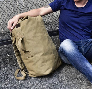 Male model sitting with the canvas rucksack next to him on the ground. 